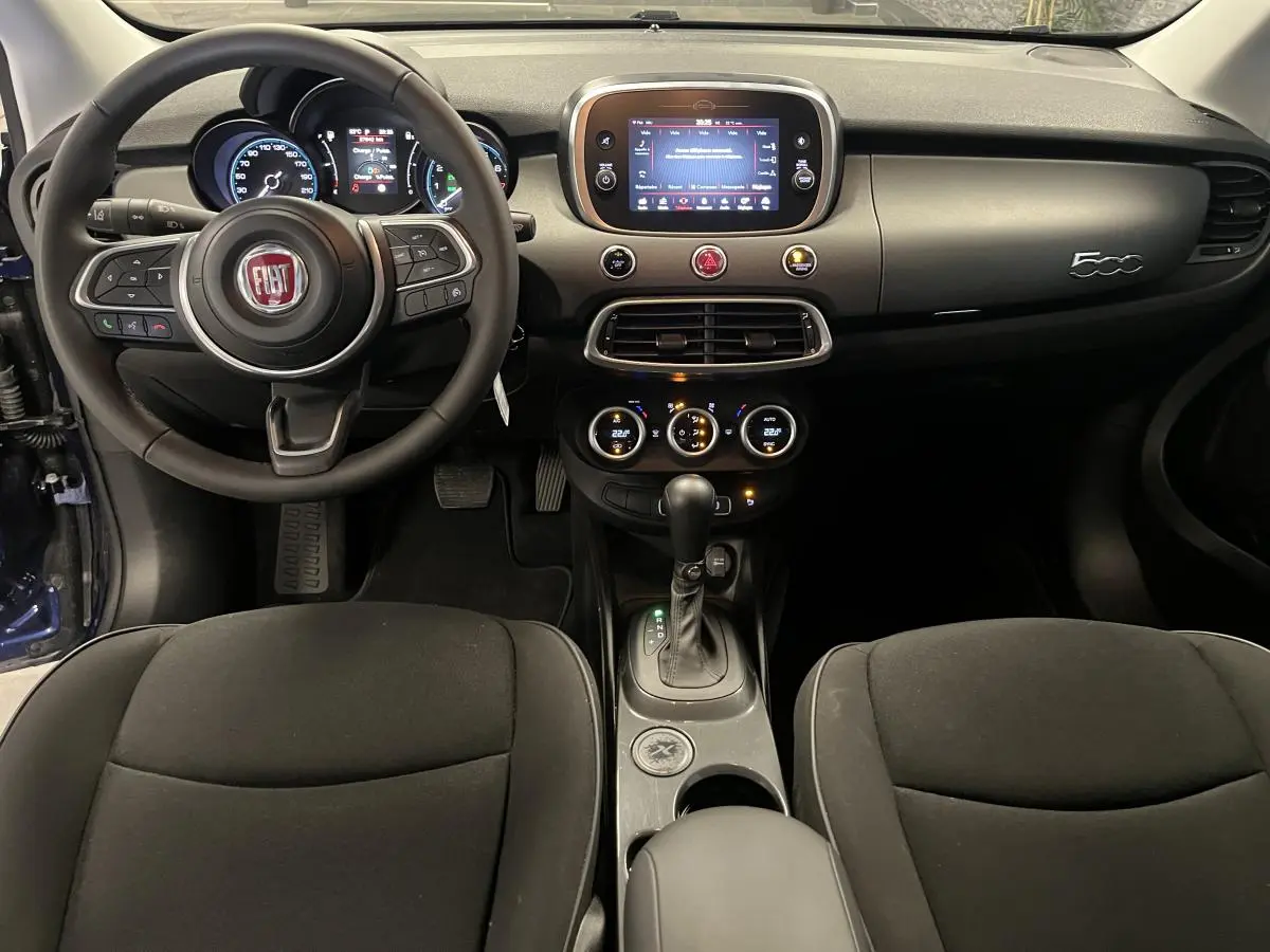 Intérieur de la Fiat 500X 2024 vu de face, avec tableau de bord gris titane et écran tactile central allumé.