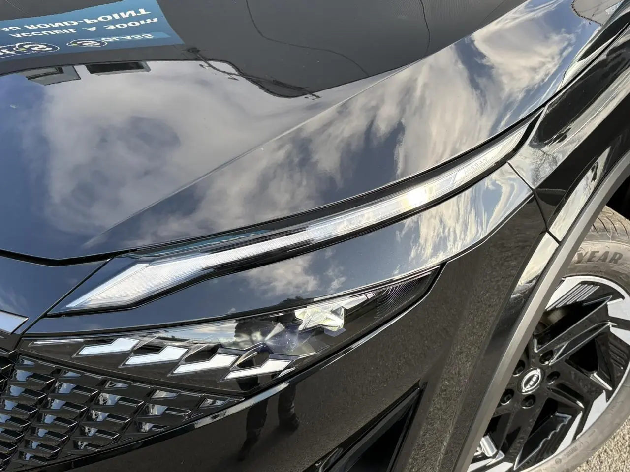 Gros plan sur le phare avant gauche noir brillant du Nissan Qashqai 2025 avec jante alliage et détails LED distinctifs.