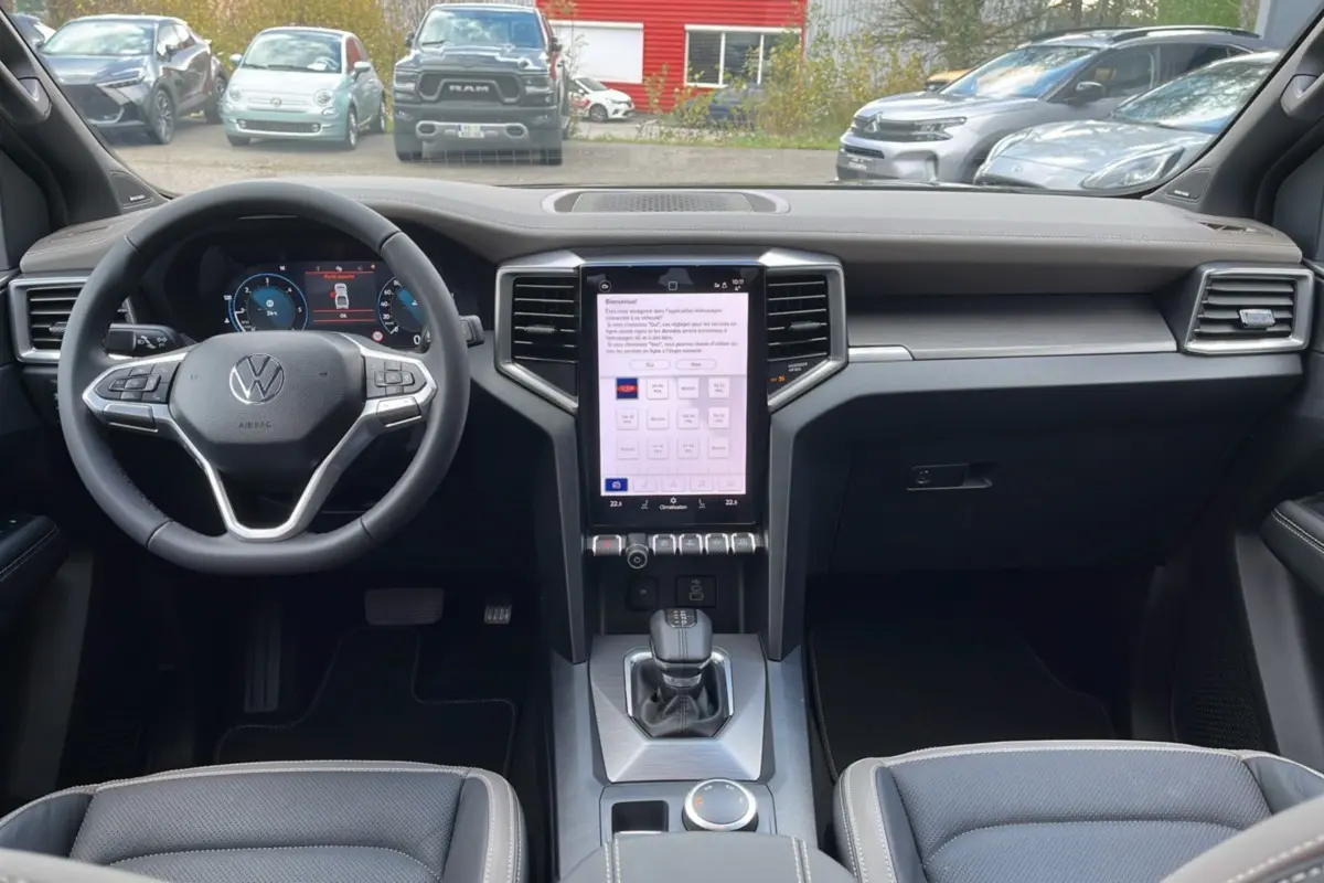 Vue intérieure avant du Volkswagen Amarok Simple Cabine 2025, tableau de bord moderne avec écran tactile vertical et volant cuir noir.