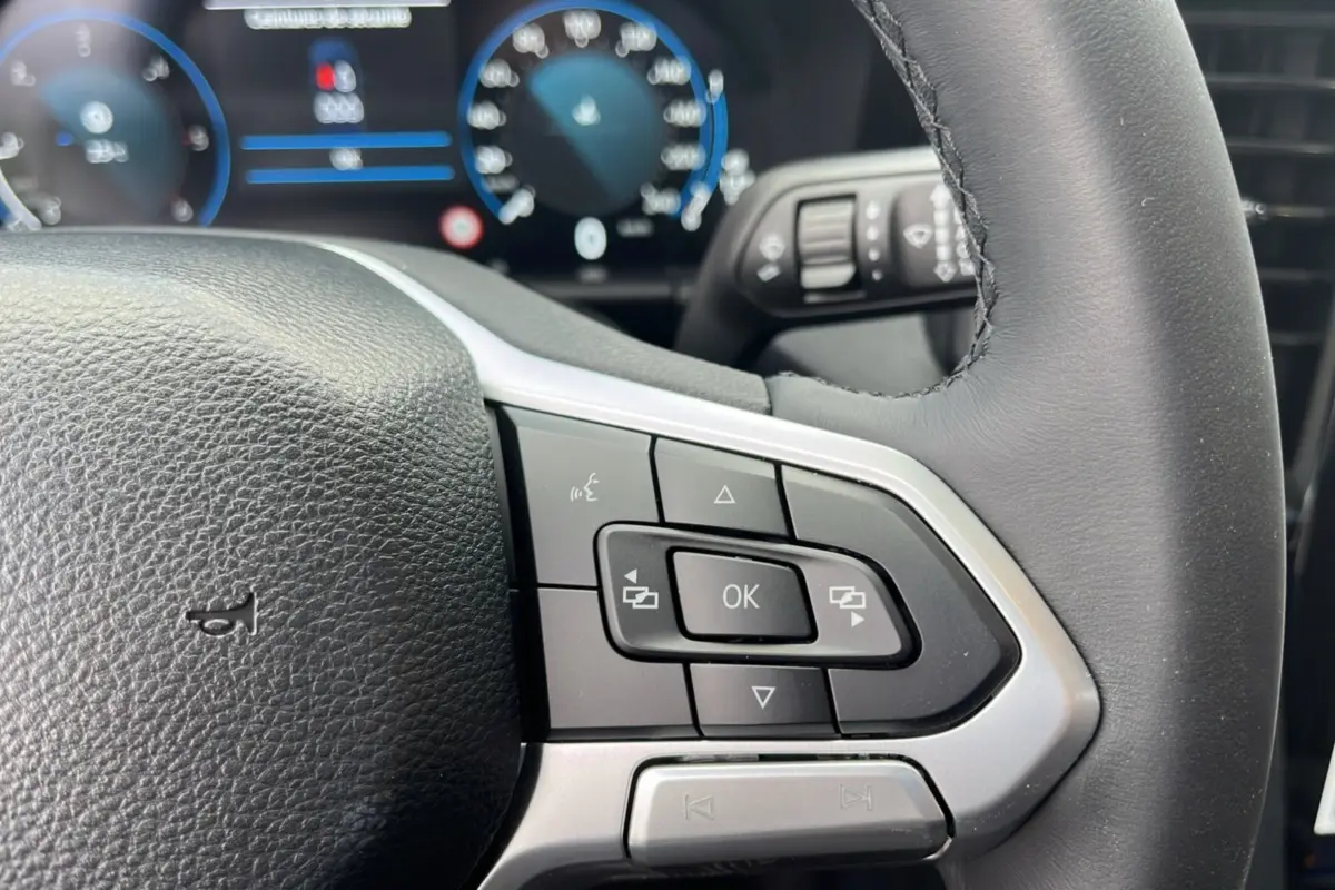 Gros plan sur le volant cuir multifonctions noir du Volkswagen Amarok V6 240 BVA10 Aventura avec commandes intégrées.