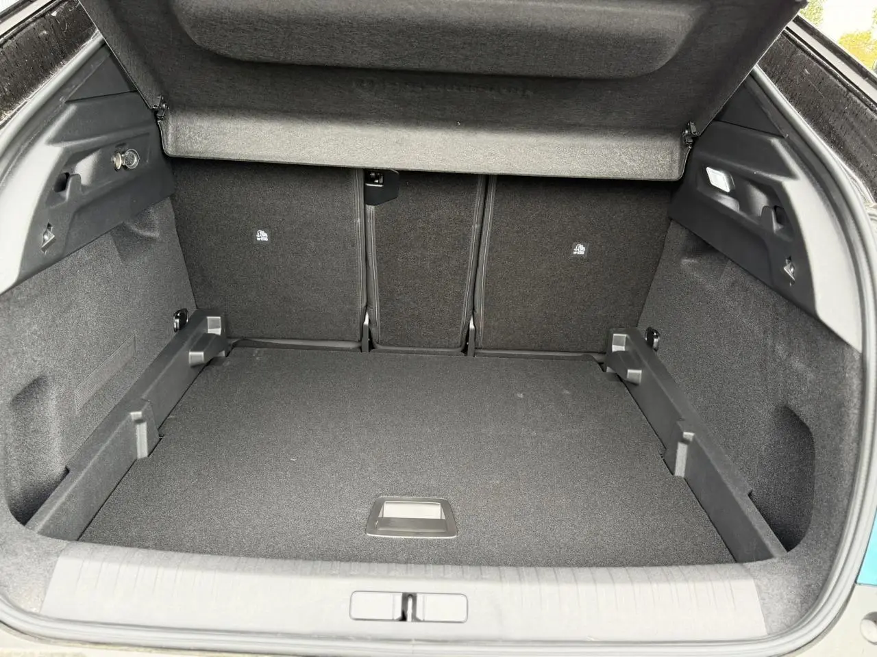 Coffre ouvert vu de l'arrière d'un Peugeot 3008 Hybrid bleu Obsession avec intérieur noir et cache-bagages relevé.