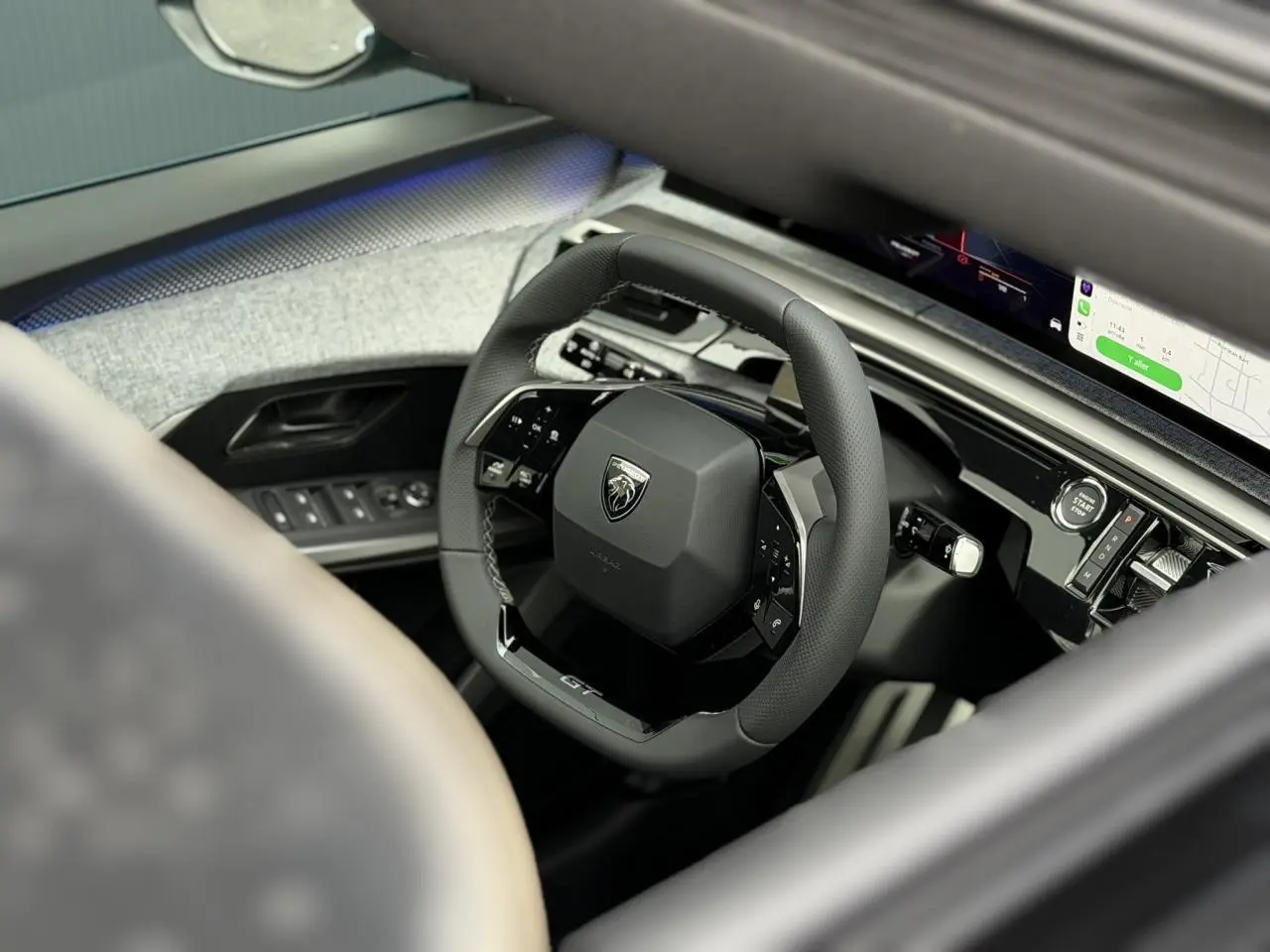 Vue intérieure rapprochée du volant compact cuir noir GT du Peugeot 3008 Hybrid 2026 avec tableau de bord numérique incurvé.
