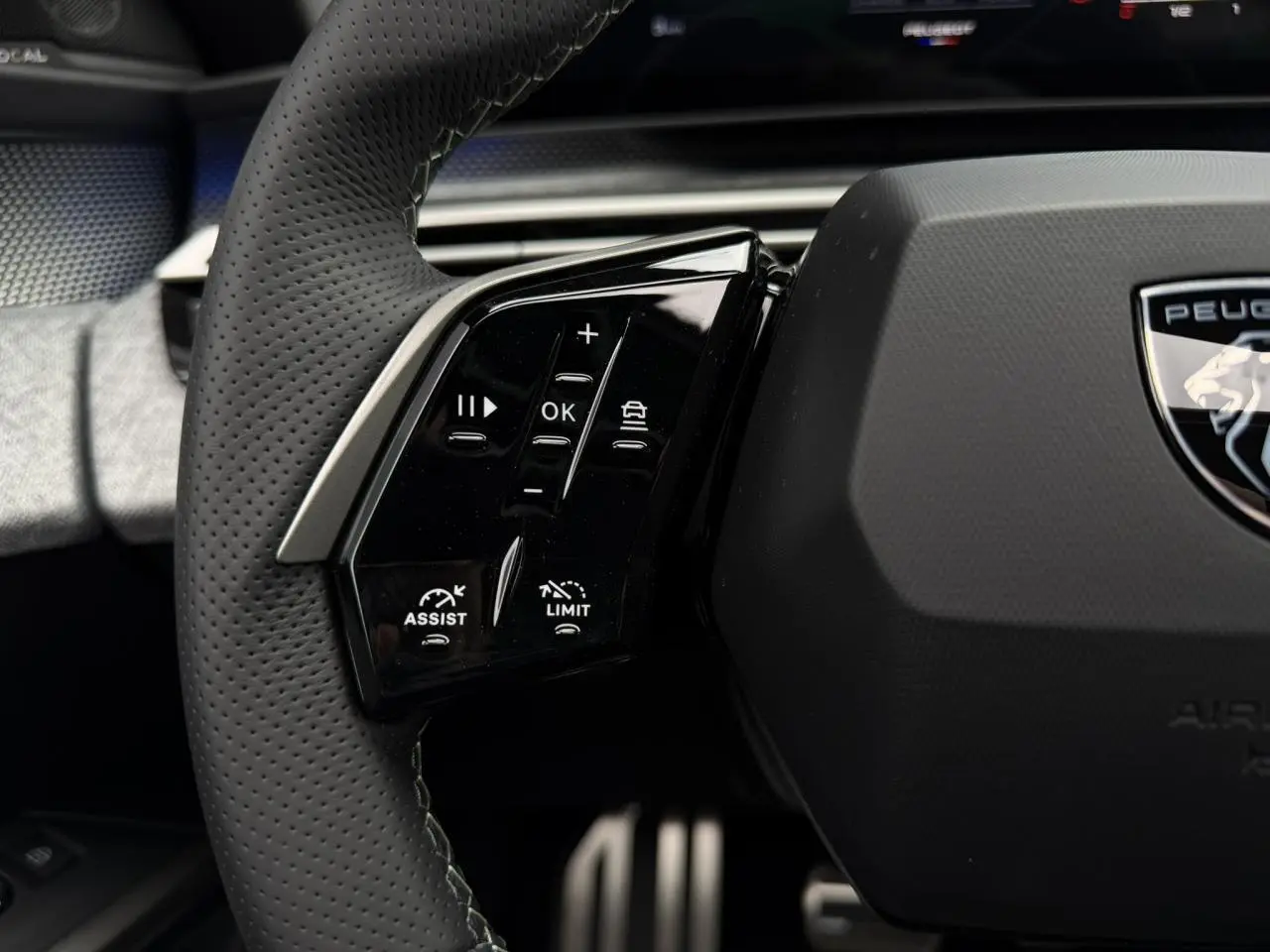 Gros plan sur le volant cuir perforé noir du Peugeot 3008 Hybrid GT avec commandes intégrées et logo Peugeot central.