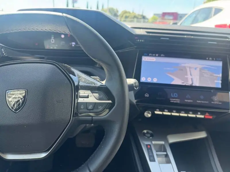 Vue intérieure centrée sur le volant noir et l’écran tactile du tableau de bord de la Peugeot 308 gris 2025 Hybrid Allure.