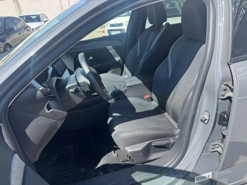 Intérieur avant droit de la Peugeot 308 gris 2025, montrant sièges tissu, volant et tableau de bord moderne.