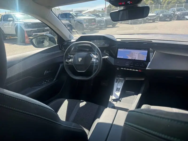 Vue intérieure avant de la Peugeot 308 Hybrid 145 gris, mettant en valeur le cockpit numérique et l'écran tactile central.
