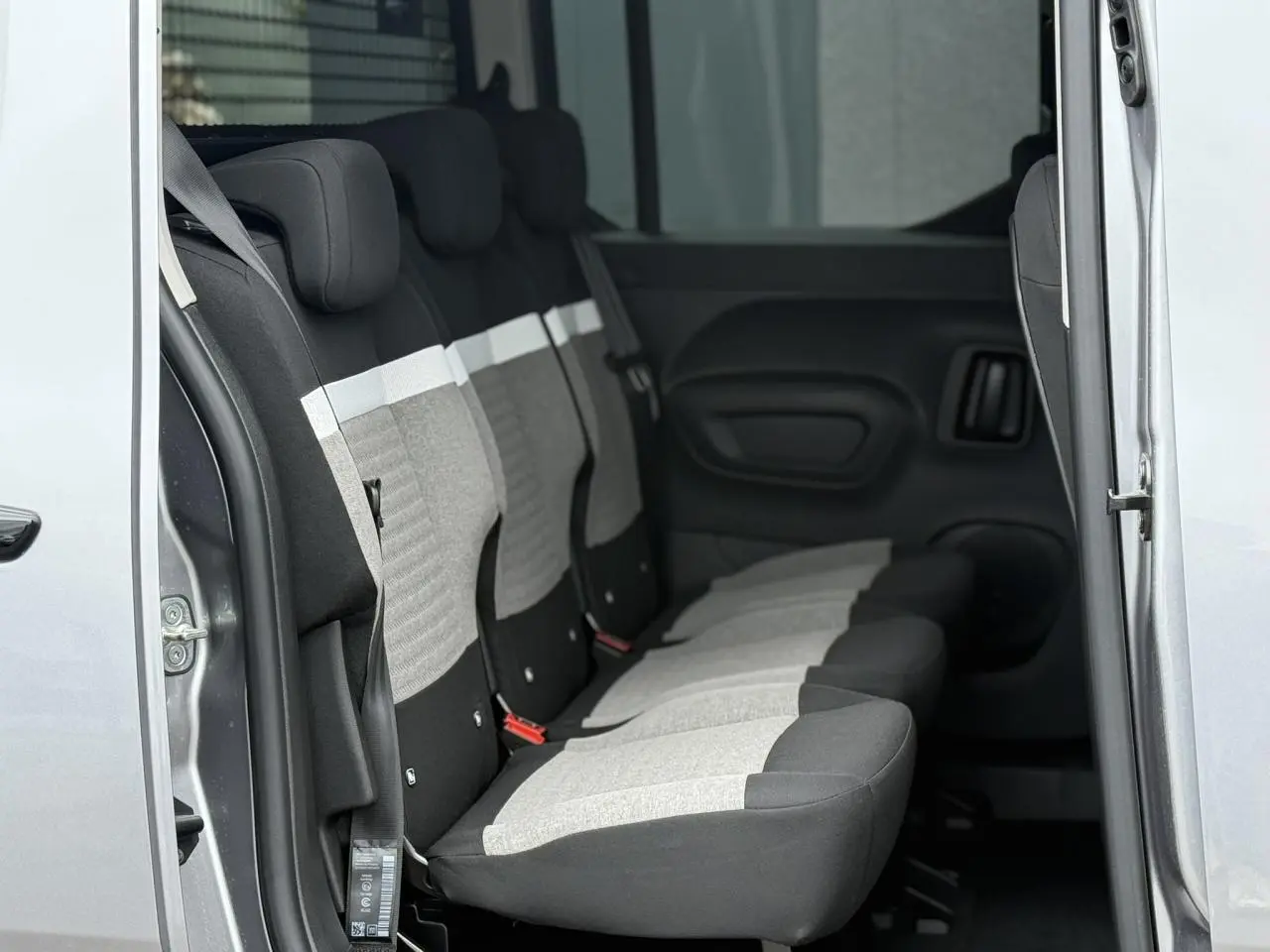Vue latérale intérieure sur les trois sièges arrière gris clair et foncé du Citroën Berlingo Multispace 2026 avec porte coulissante ouverte.