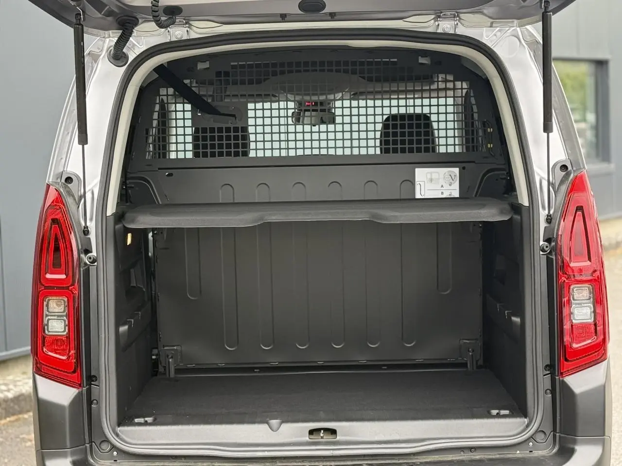 Vue arrière ouverte du Citroën Berlingo Multispace gris acier, montrant le coffre vide et la grille de séparation intérieure.