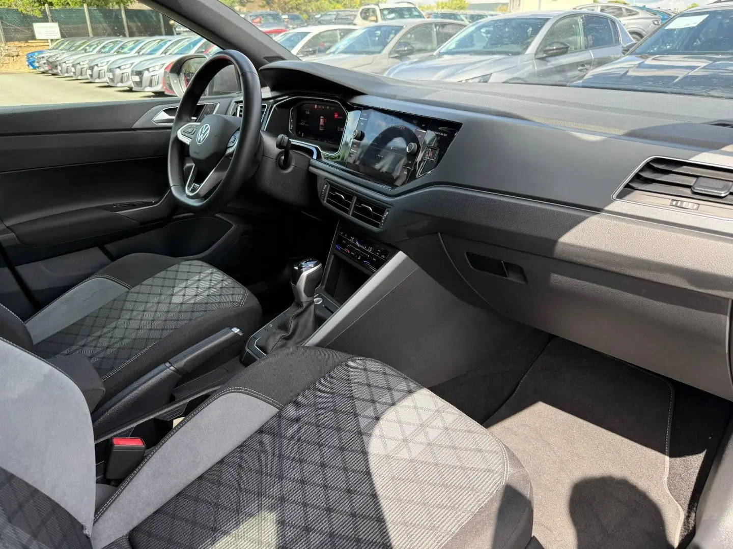 Vue intérieure côté passager avant du Volkswagen Taigo 2025, montrant le tableau de bord et les sièges en tissu gris à motif.
