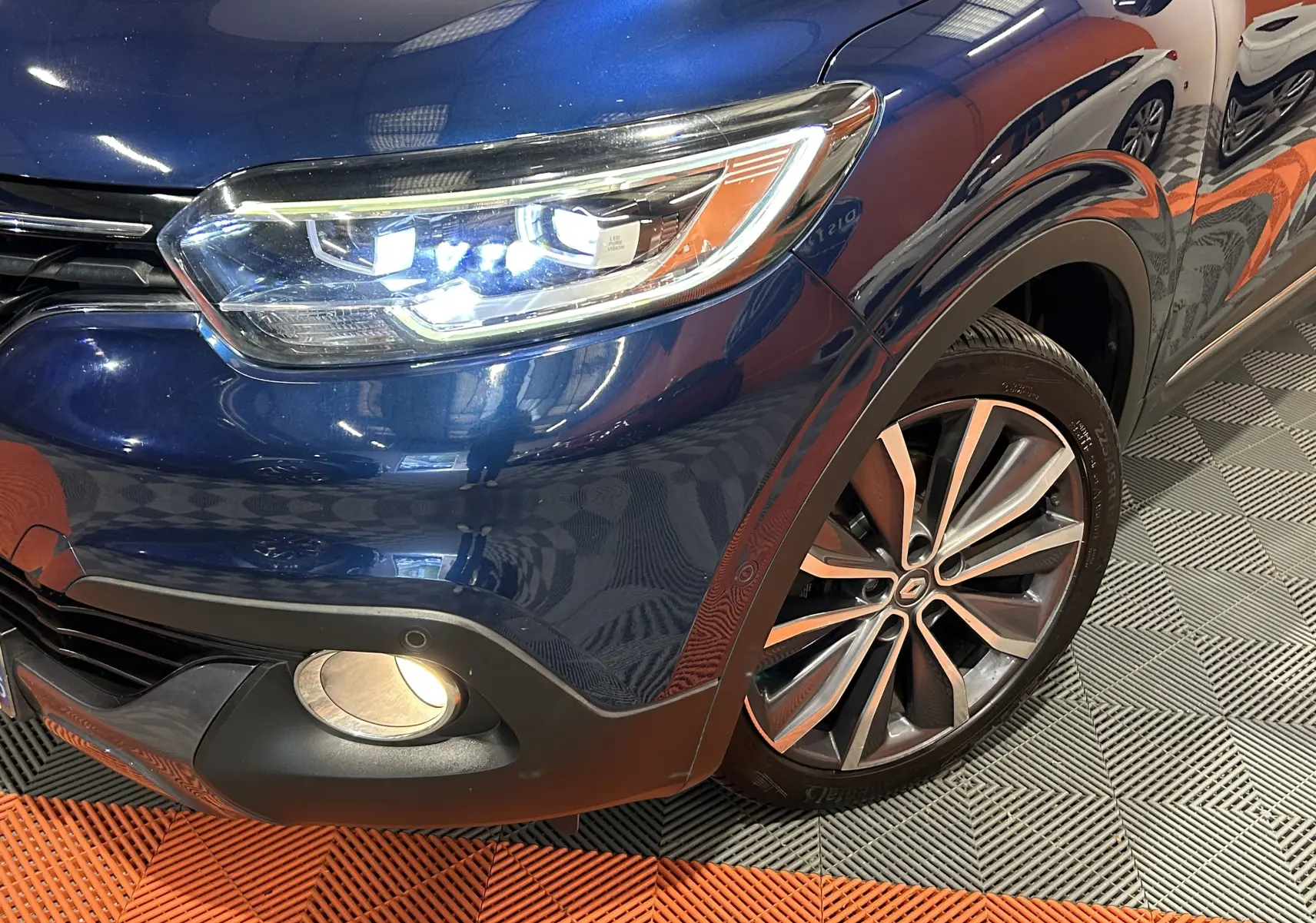 Gros plan sur l'avant droit bleu du Renault Kadjar TCe 130 Intens avec phares LED allumés et jante alliage bicolore.