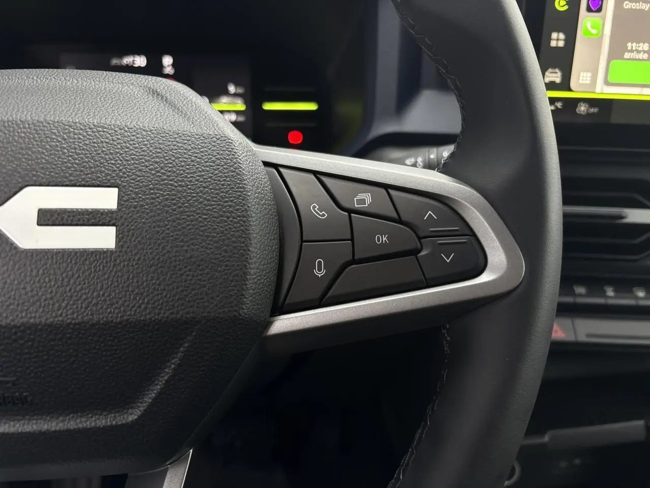 Gros plan sur les commandes au volant côté droit du Dacia Duster blanc glacier, avec écran tactile en arrière-plan.