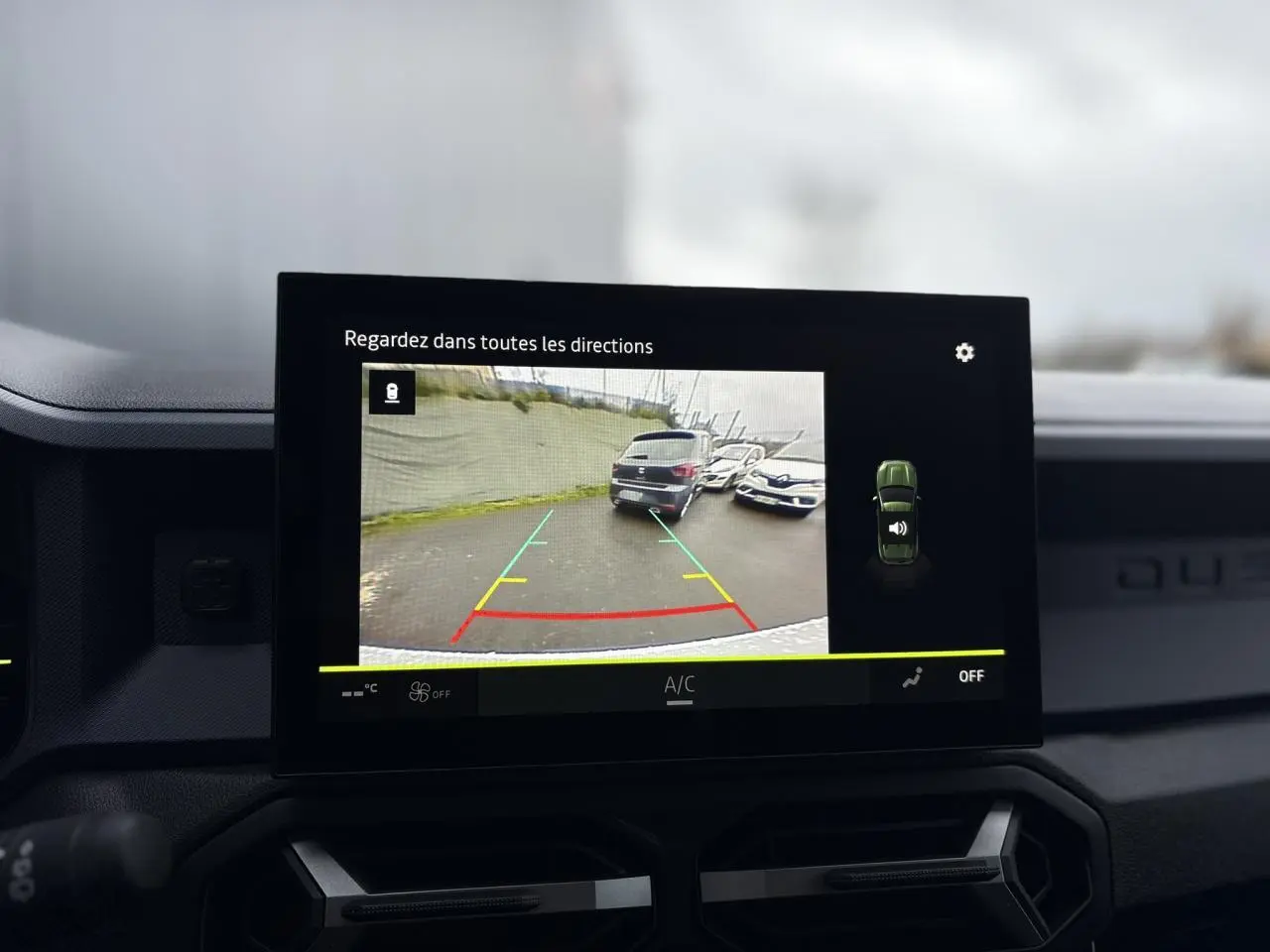 Écran tactile du Dacia Duster blanc Glacier montrant la caméra de recul avec vue arrière et lignes de guidage colorées.