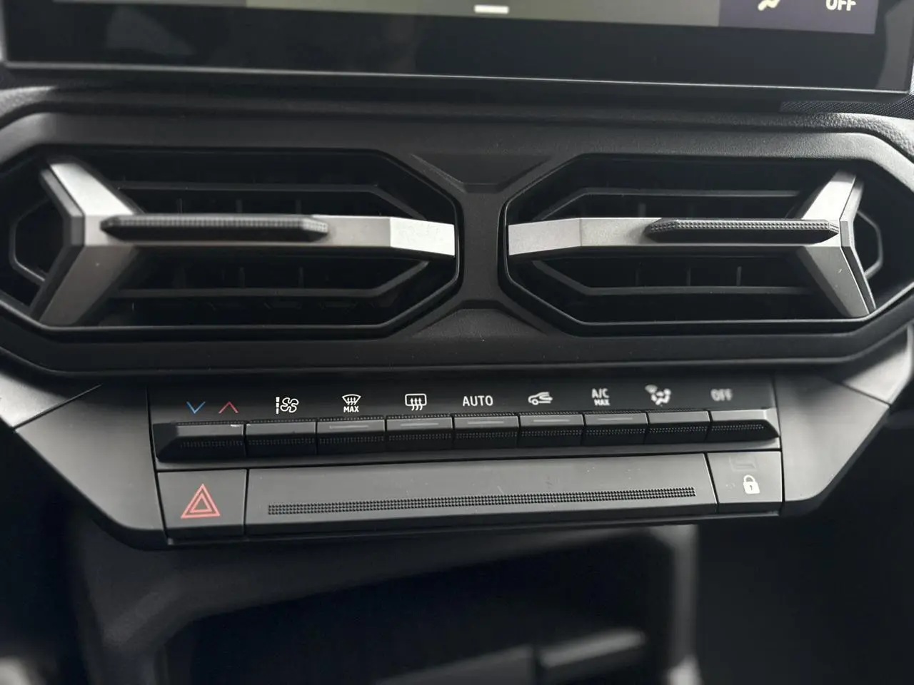 Détail des commandes de climatisation et aérateurs hexagonaux noirs du tableau de bord du Dacia Duster blanc Glacier 2025.
