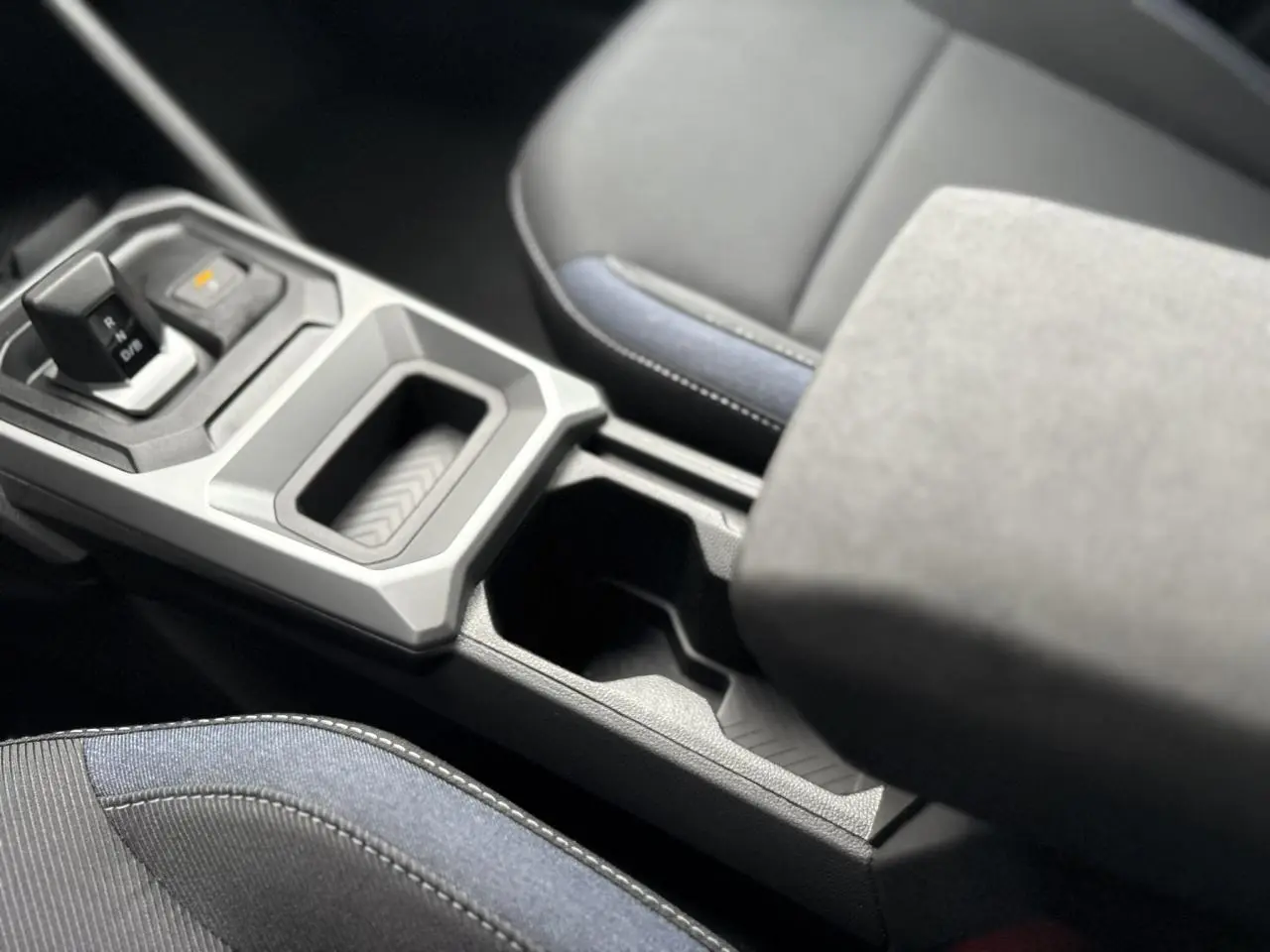 Gros plan sur la console centrale et le levier de vitesse du Dacia Duster blanc Glacier, avec accoudoir et sièges tissu noir et bleu.