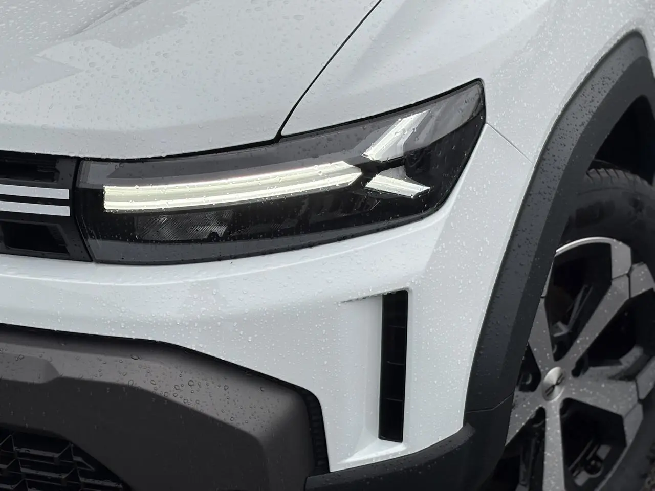 Gros plan sur l'avant droit du Dacia Duster blanc Glacier, mettant en valeur le phare LED et la jante alliage noire.
