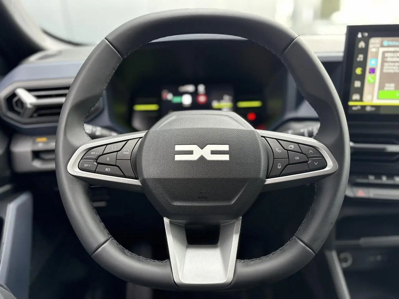 Volant noir de DACIA Duster 2025 en vue frontale, avec commandes intégrées et écran tactile en arrière-plan.