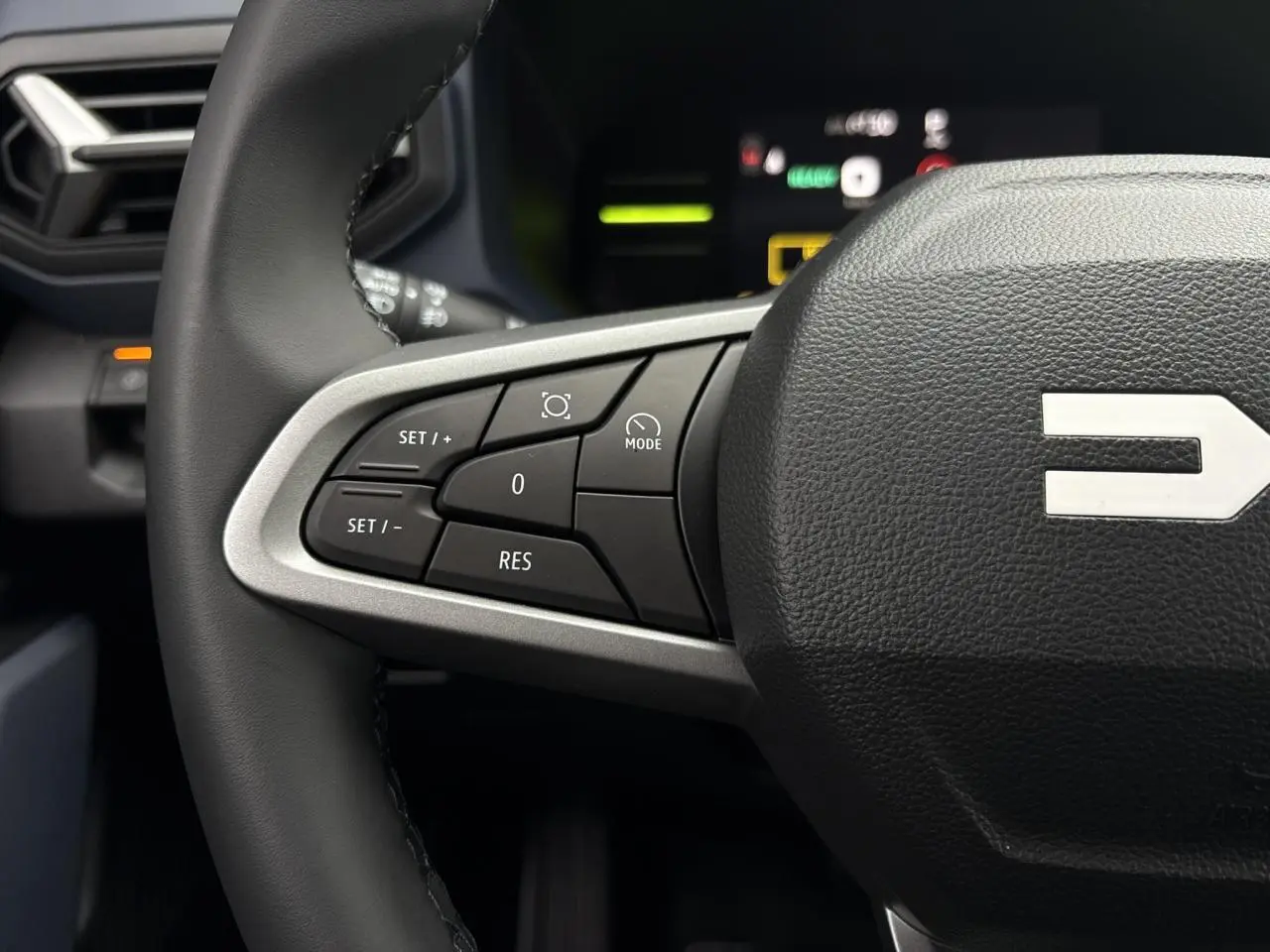 Gros plan sur le volant noir du Dacia Duster 2025, montrant les commandes de régulateur de vitesse côté gauche.