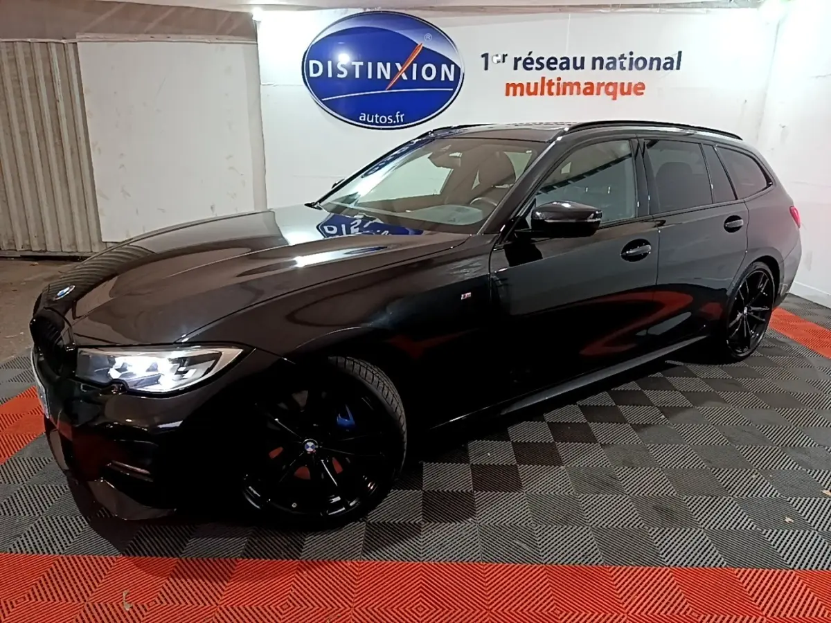 BMW Série 3 318i M Sport noire vue en 3/4 avant droit avec jantes noires et phares allumés dans un showroom