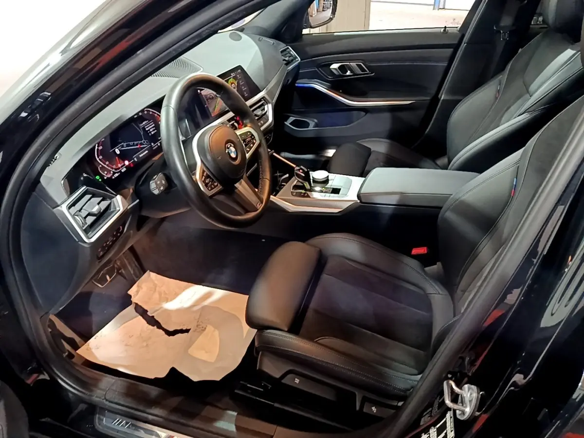 Intérieur noir de BMW Série 3 318i 2022, vue côté conducteur montrant sièges cuir et tableau de bord digital.