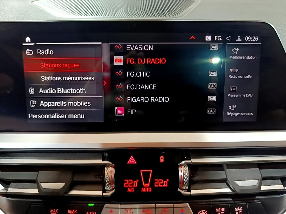 Vue rapprochée de l'écran tactile central et commandes de climatisation rougeoyant d'une BMW Série 3 noire 318i M Sport 2022.