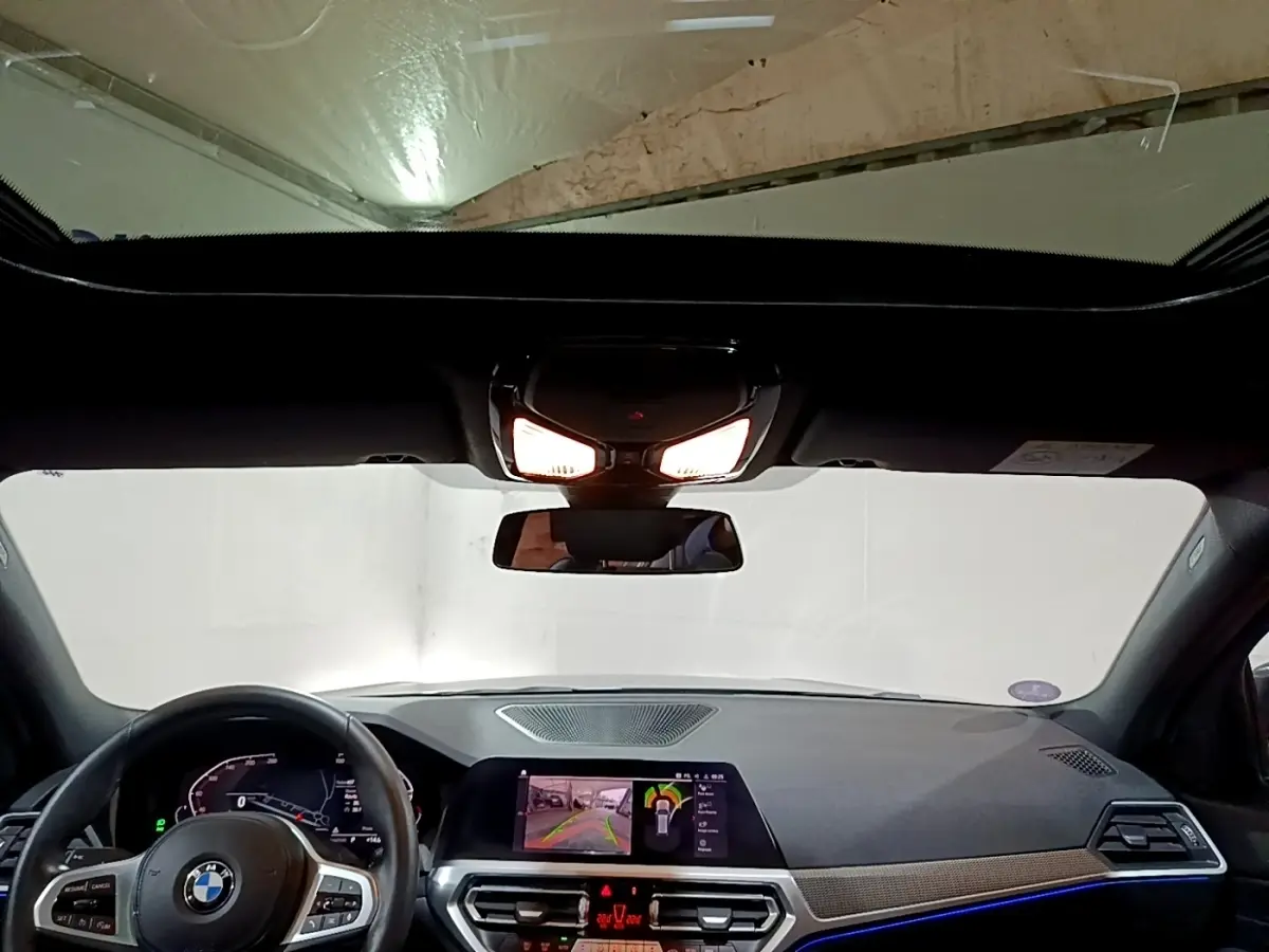 Vue intérieure avant du tableau de bord et volant cuir d’une BMW Série 3 318i noir avec écran tactile et éclairage d’ambiance bleu.