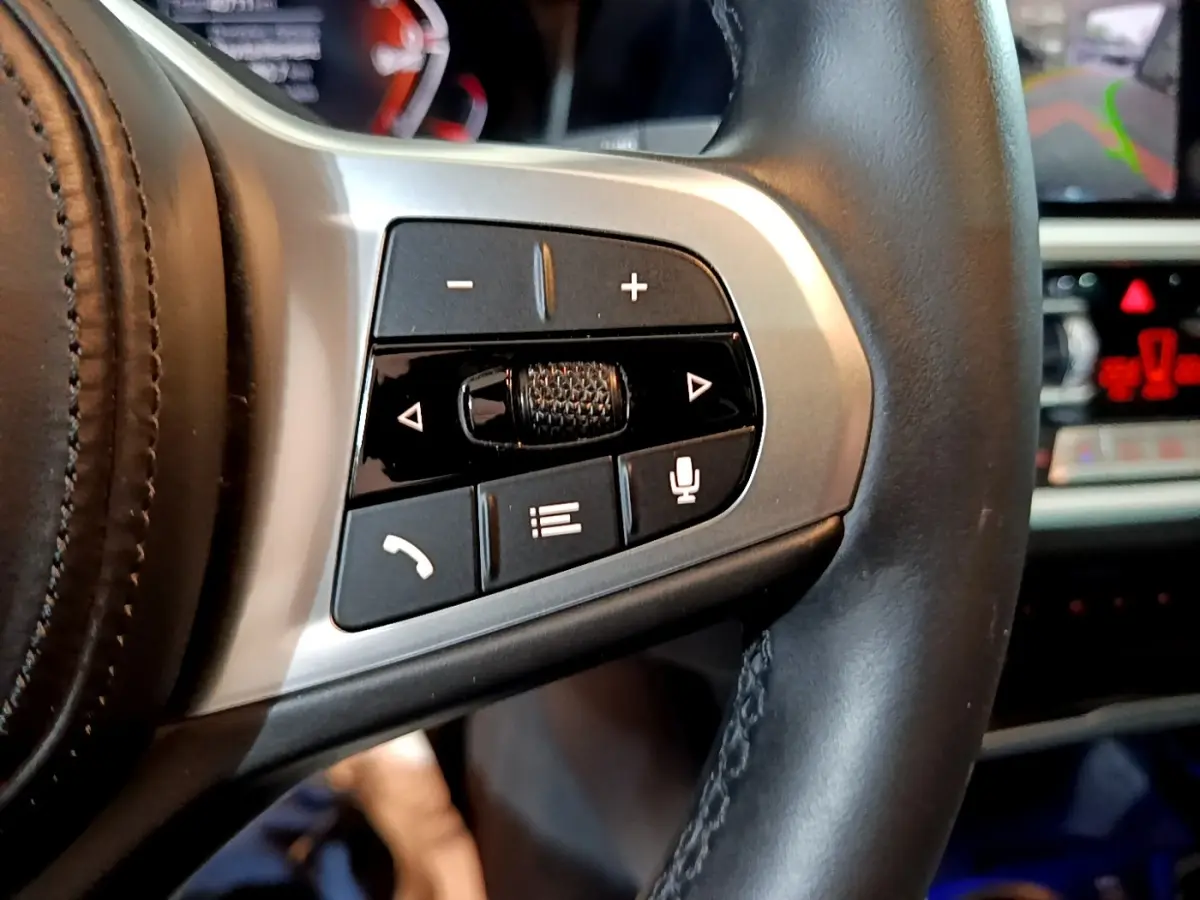 Gros plan sur les commandes du volant en cuir noir de la BMW Série 3 318i M Sport 2022 avec tableau de bord en arrière-plan.