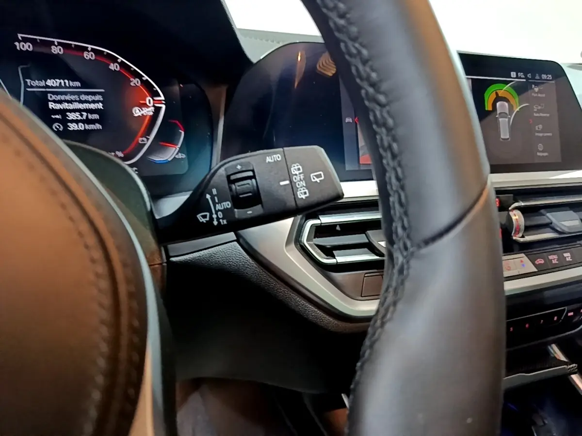 Gros plan sur le tableau de bord digital et le volant cuir noir d'une BMW Série 3 318i 2022 avec affichage multifonctions.