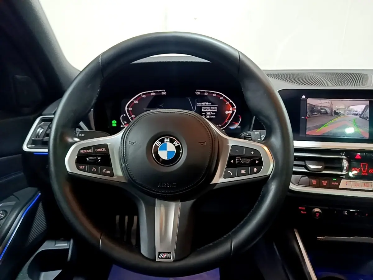 Vue rapprochée du volant cuir noir M Sport de la BMW Série 3 318i avec tableau de bord digital et écran de caméra de recul.