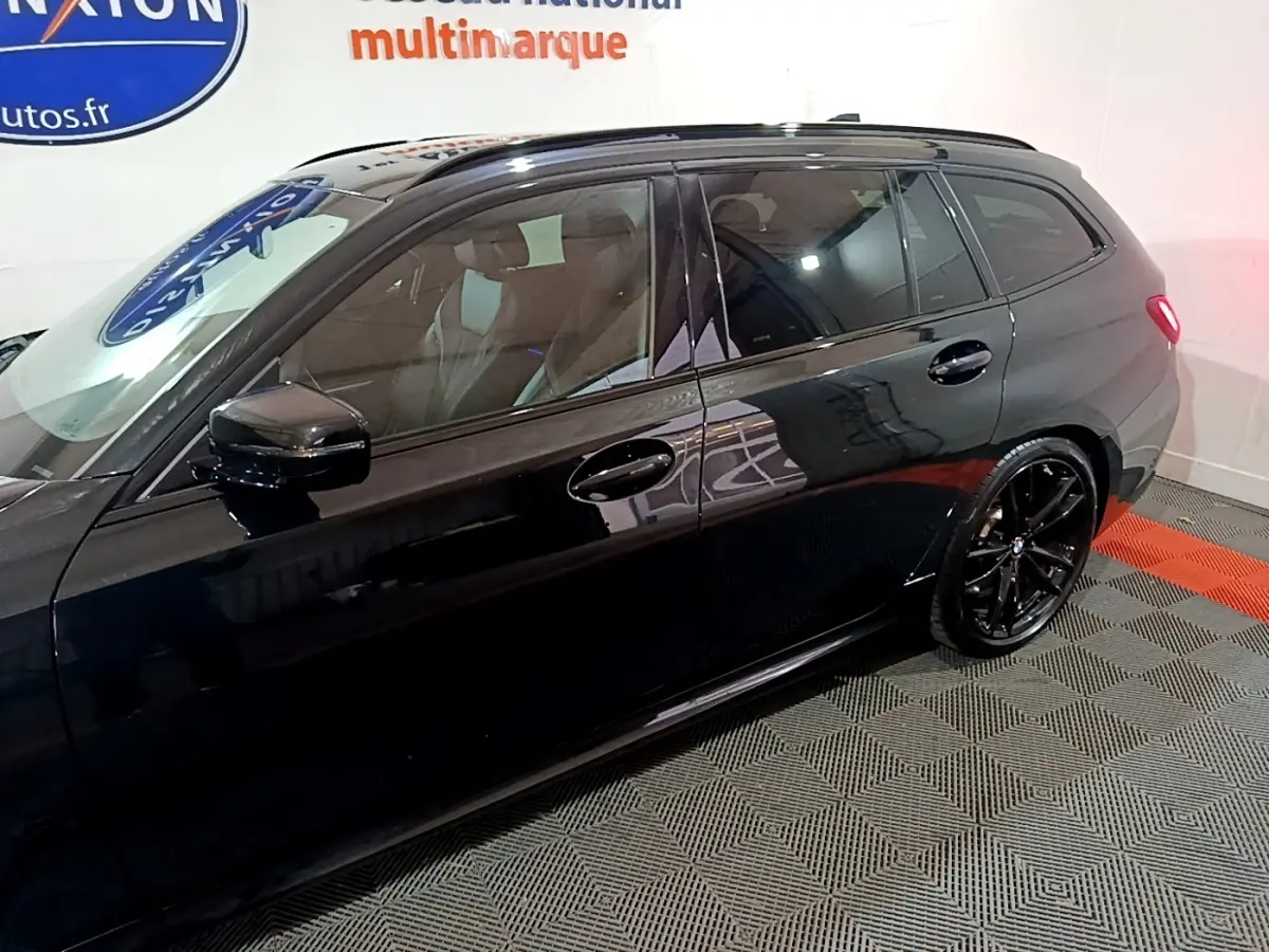 Profil côté gauche d'une BMW Série 3 noire 318i M Sport avec jantes noires et vitres teintées en intérieur showroom.