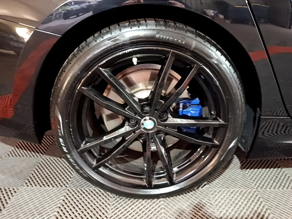 Gros plan sur la jante noire brillante et l'étrier de frein bleu de la BMW Série 3 noire côté arrière droit.