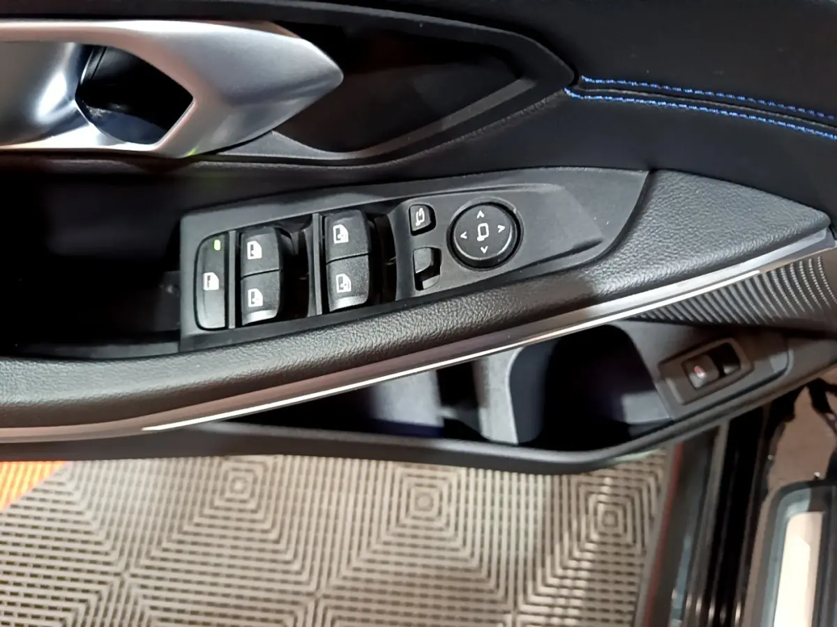 Gros plan sur la commande des vitres et rétroviseurs côté conducteur d’une BMW Série 3 noire avec surpiqûres bleues.