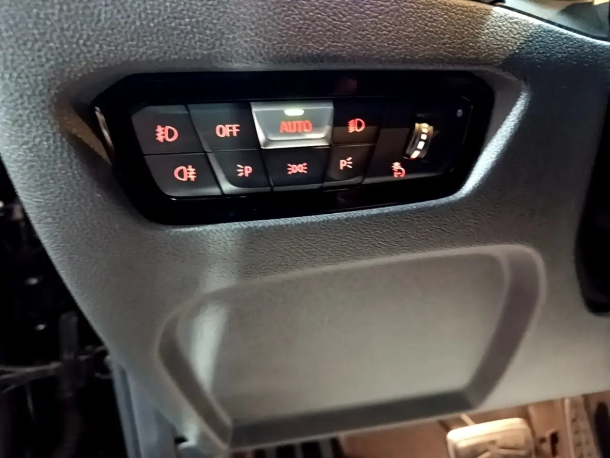 Gros plan sur le panneau de commande d'éclairage noir avec boutons rétroéclairés rouges dans une BMW Série 3 318i 2022.