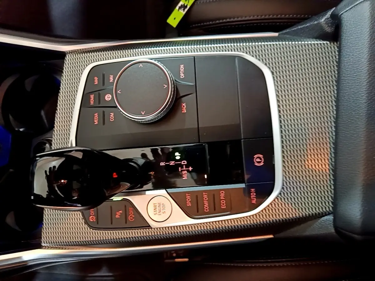 Gros plan sur la console centrale de la BMW Série 3 noire, mettant en valeur le levier de vitesses et les commandes de mode de conduite.