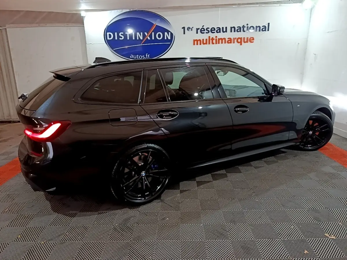 BMW Série 3 318i M Sport noir vue de profil côté gauche en intérieur avec jantes noires et feux arrière allumés