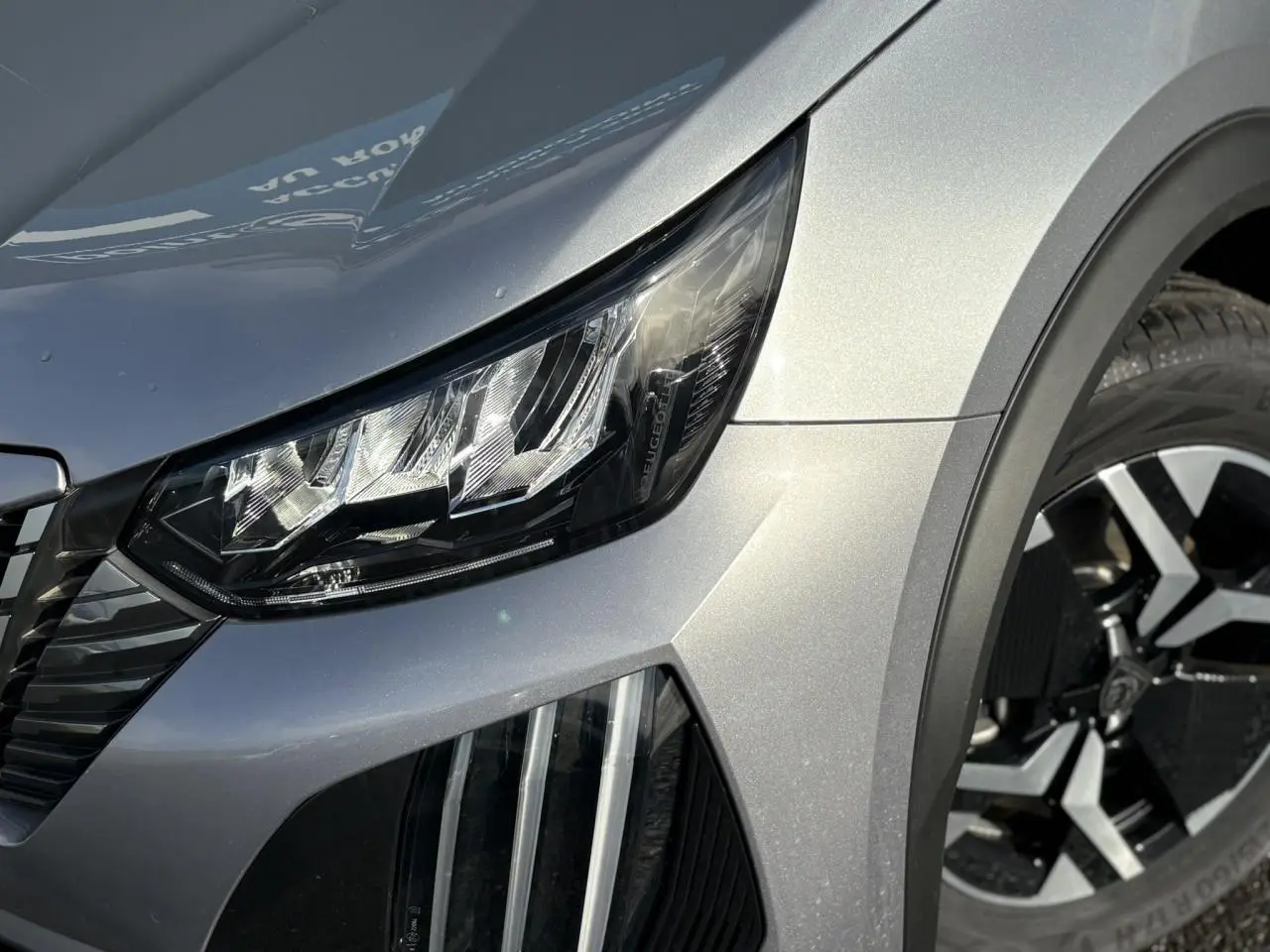 Gros plan sur le phare avant droit et la jante alliage 17'' diamantée du Peugeot 2008 Hybrid 145 gris Artense.