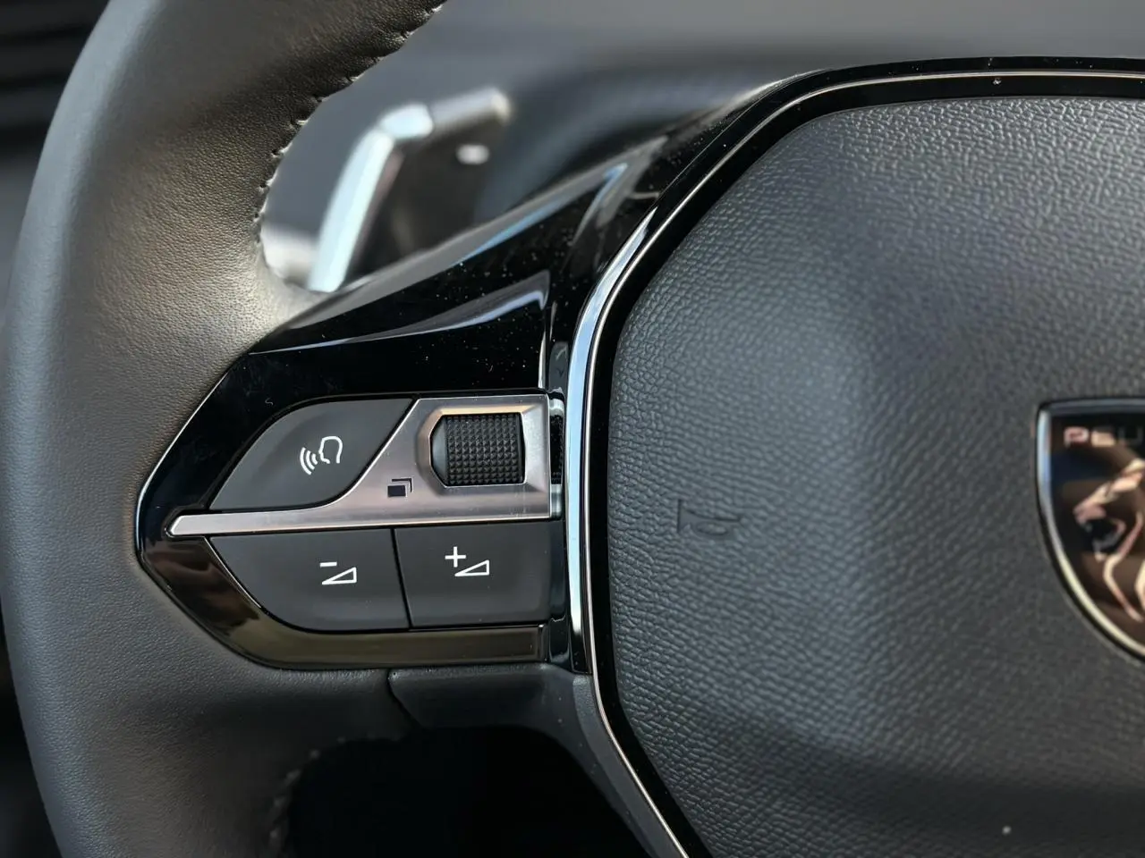 Gros plan sur les commandes multimédia gauche du volant cuir noir du Peugeot 2008 Hybrid 145 e-DSC6 Allure 2025.