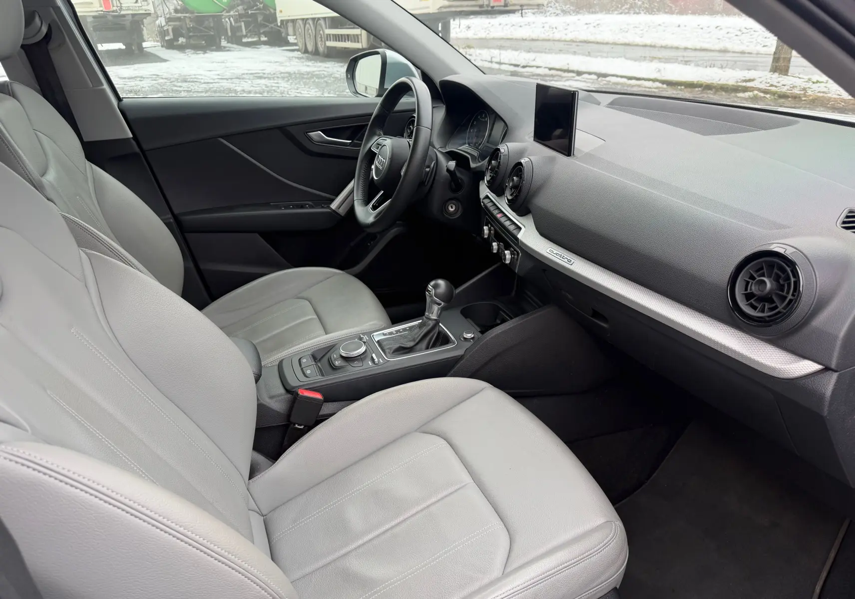 Vue intérieure côté conducteur de l'Audi Q2 2017 avec sellerie gris clair en similicuir et tableau de bord moderne.