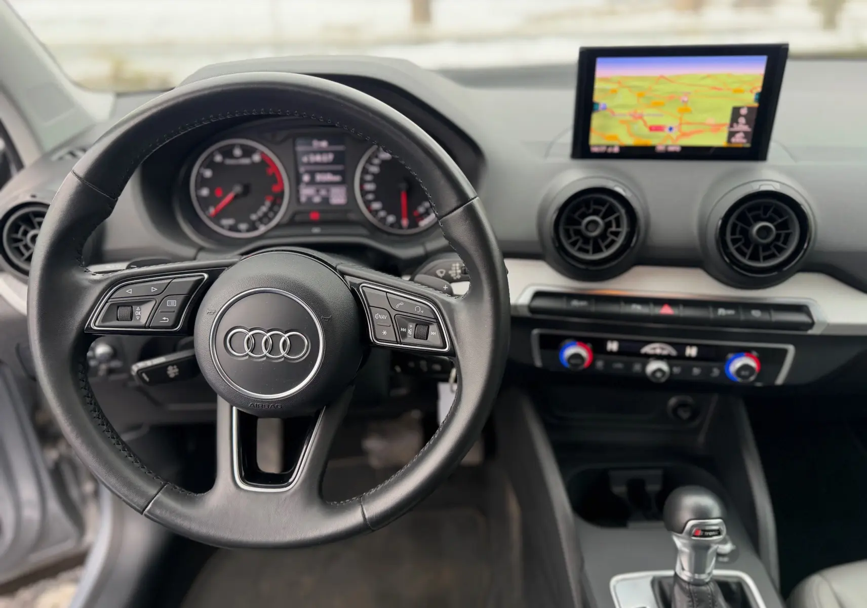 Vue intérieure centrée sur le volant noir d’un Audi Q2 2017 avec tableau de bord et écran GPS en arrière-plan.