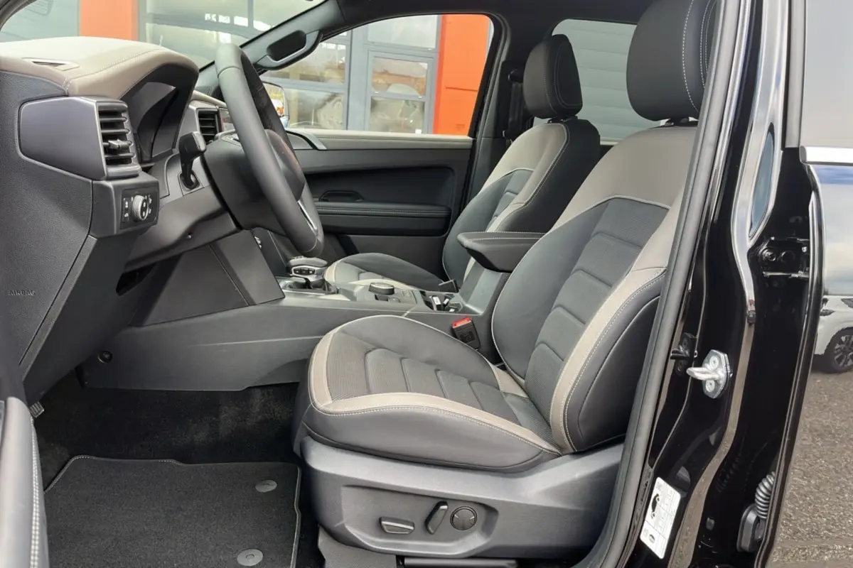 Vue intérieure côté conducteur du Volkswagen Amarok Simple Cabine noir 2025, sièges cuir bi-ton et commandes électriques visibles.