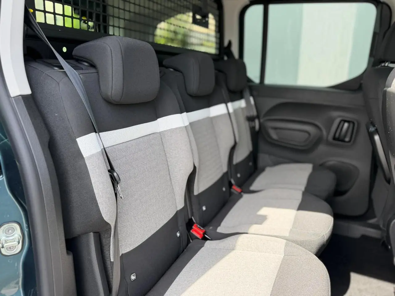 Vue latérale intérieure des trois sièges arrière gris et noirs du Citroën Berlingo Multispace avec ceinture et porte coulissante ouverte.