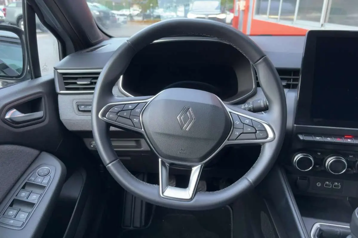 Vue intérieure centrée sur le volant cuir multifonctions de la Renault Clio 2025, avec tableau de bord et commandes visibles.