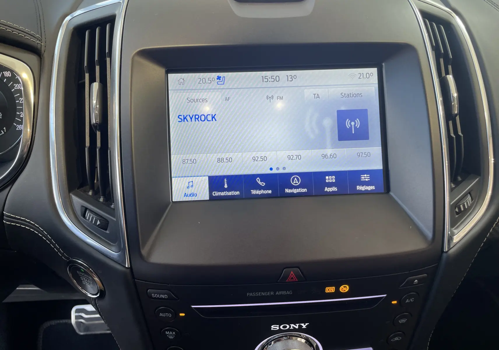 Vue rapprochée de l'écran tactile central et de la console du Ford S-MAX Vignale gris, affichant la radio Skyrock.