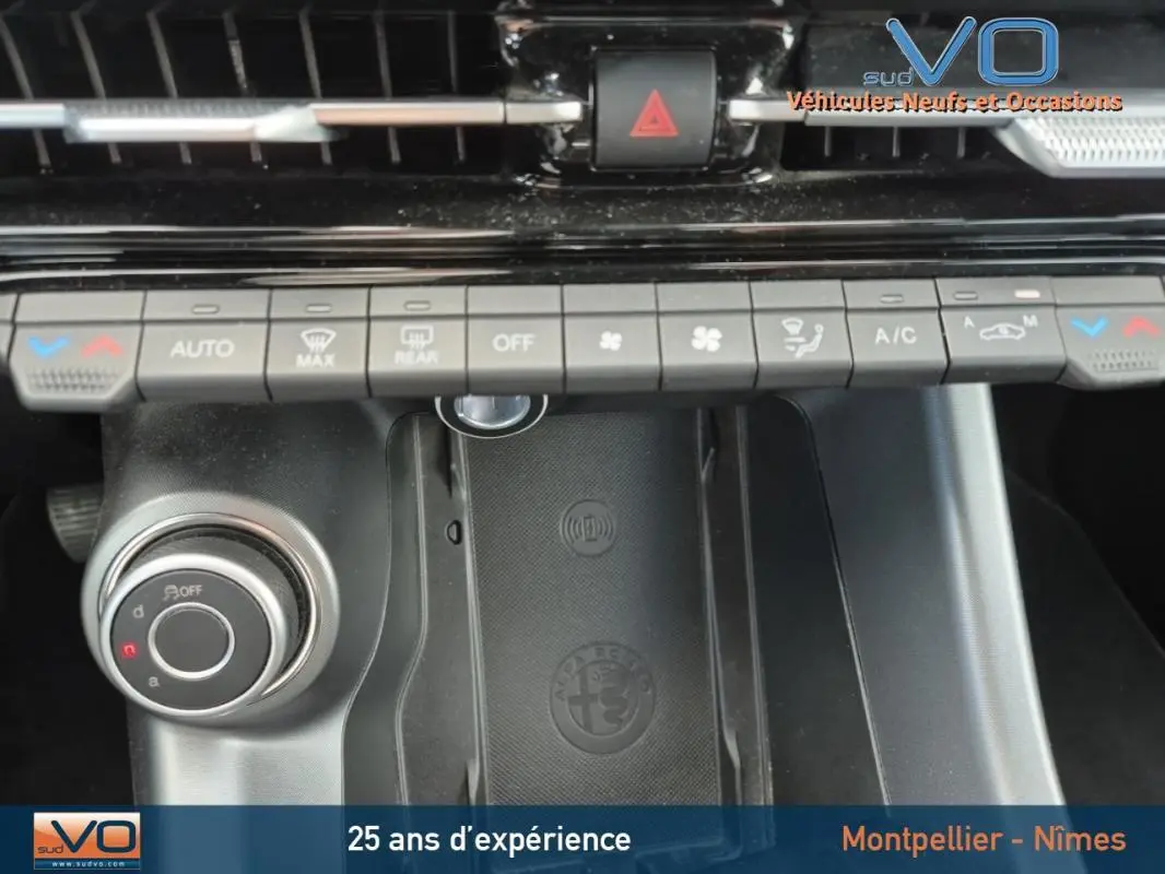 Vue rapprochée de la console centrale de l'Alfa Romeo Tonale 2023, montrant les commandes de climatisation et le chargeur sans fil noir avec logo Alfa Romeo.