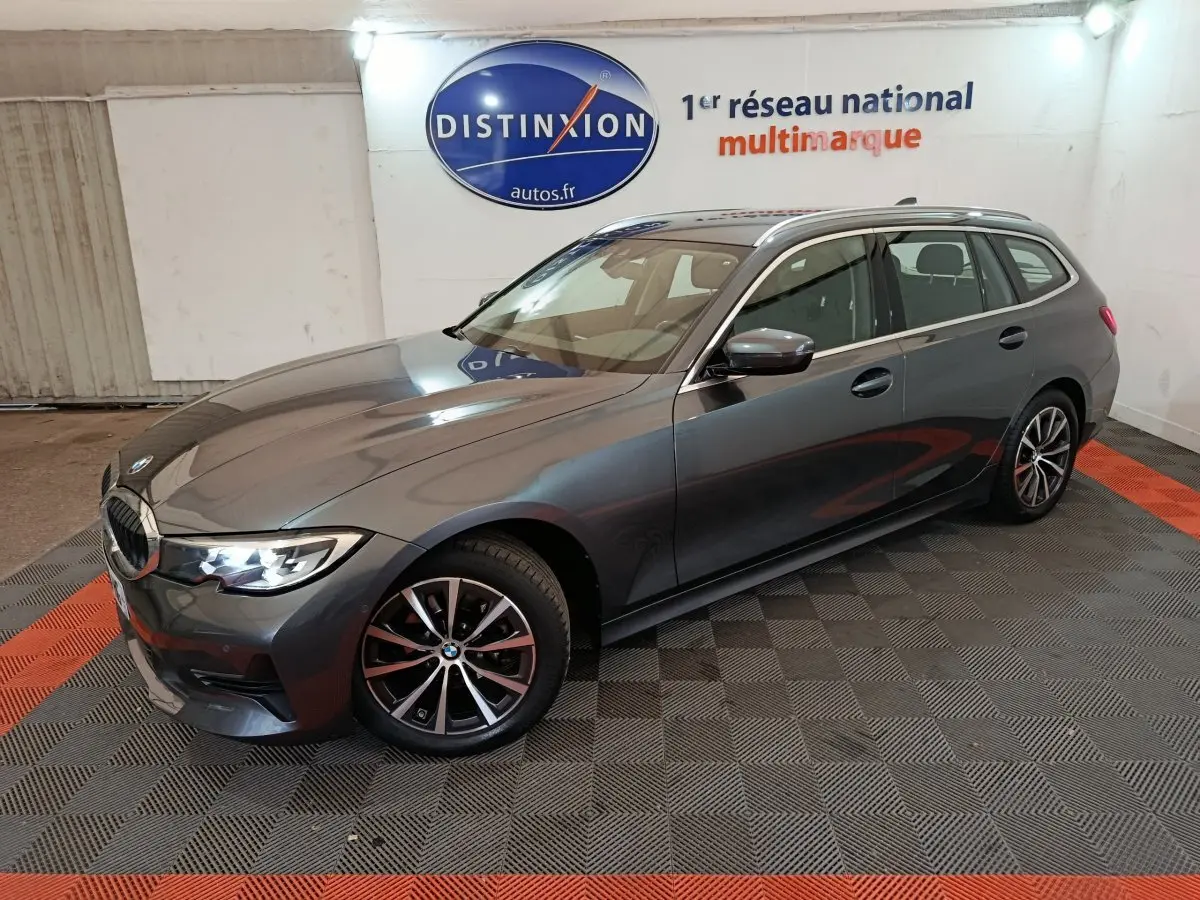BMW Série 3 316d gris clair vue 3/4 avant droit, avec jantes alliage et phares LED allumés en intérieur showroom.