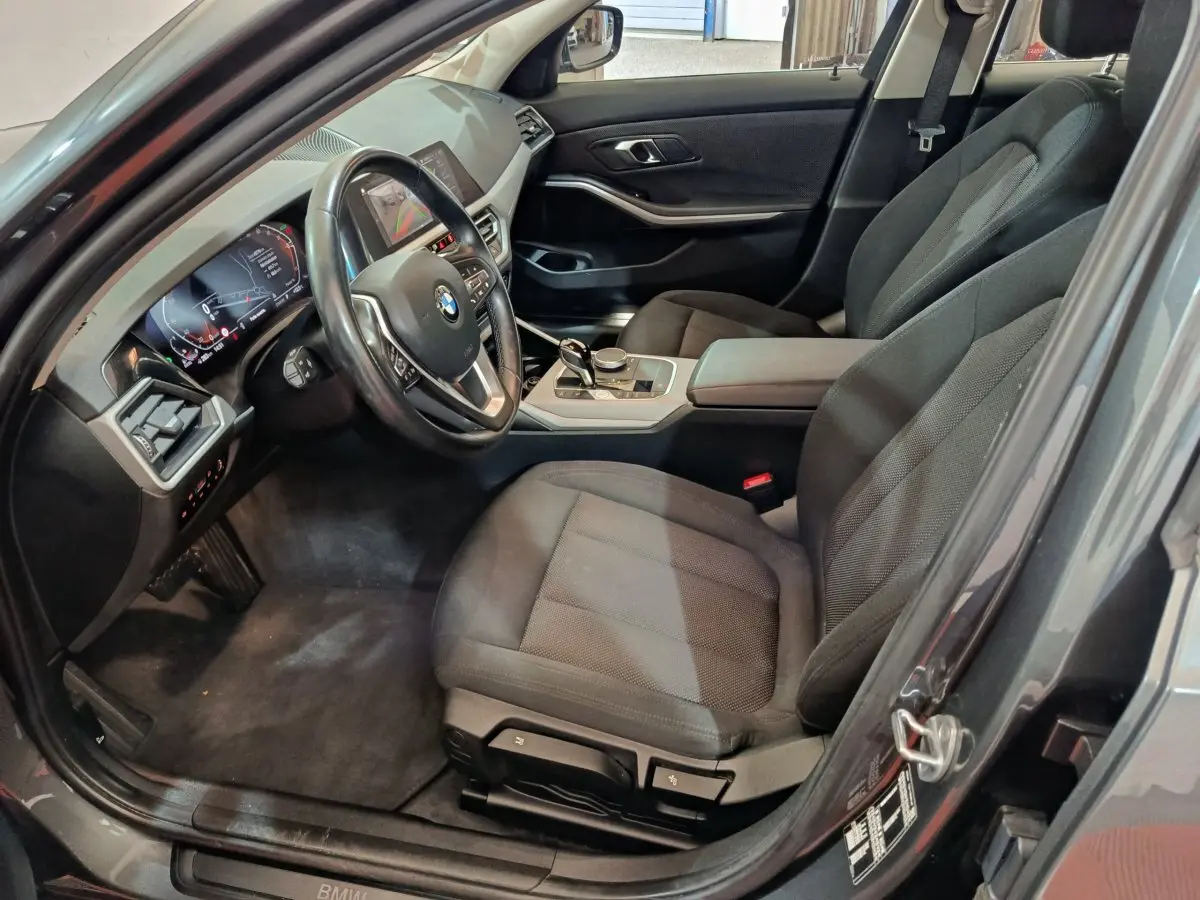 Intérieur avant droit d'une BMW Série 3 gris clair, avec tableau de bord numérique et volant cuir multifonctions.