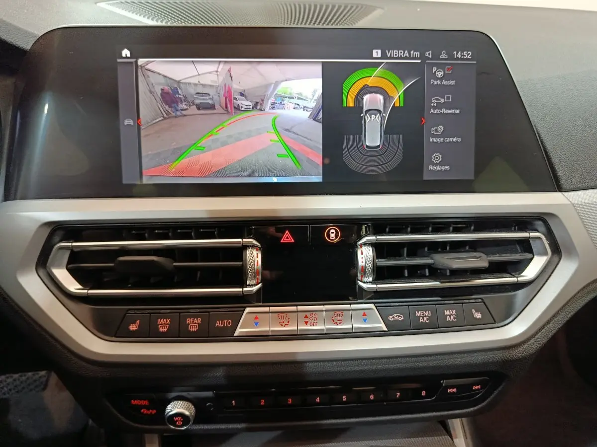 Écran tactile central avec affichage caméra de recul et commandes climatisation dans l'habitacle d'une BMW Série 3 gris clair 2022.