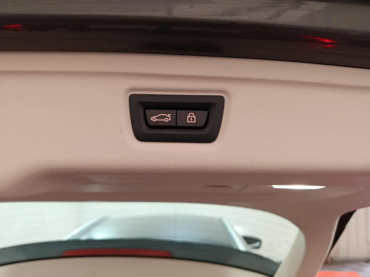 Bouton d'ouverture et de verrouillage électrique du coffre sur le hayon intérieur d'une BMW Série 3 gris clair.