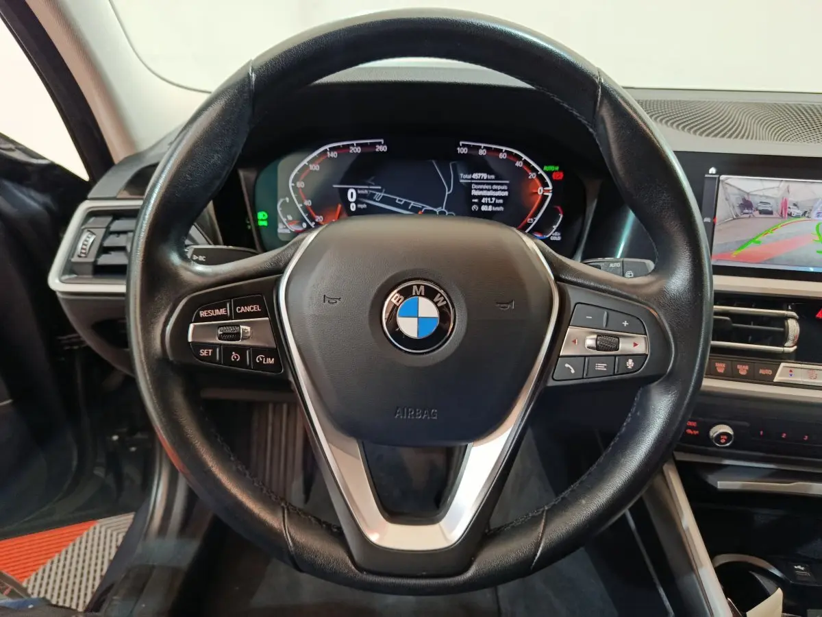 Vue rapprochée du volant cuir noir BMW Série 3 316d 2022 avec tableau de bord digital et écran tactile central.
