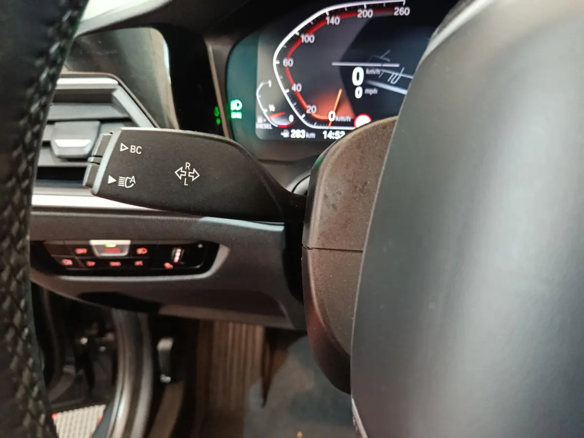 Gros plan sur le levier de clignotant et le tableau de bord numérique d'une BMW Série 3 gris clair, intérieur moderne.