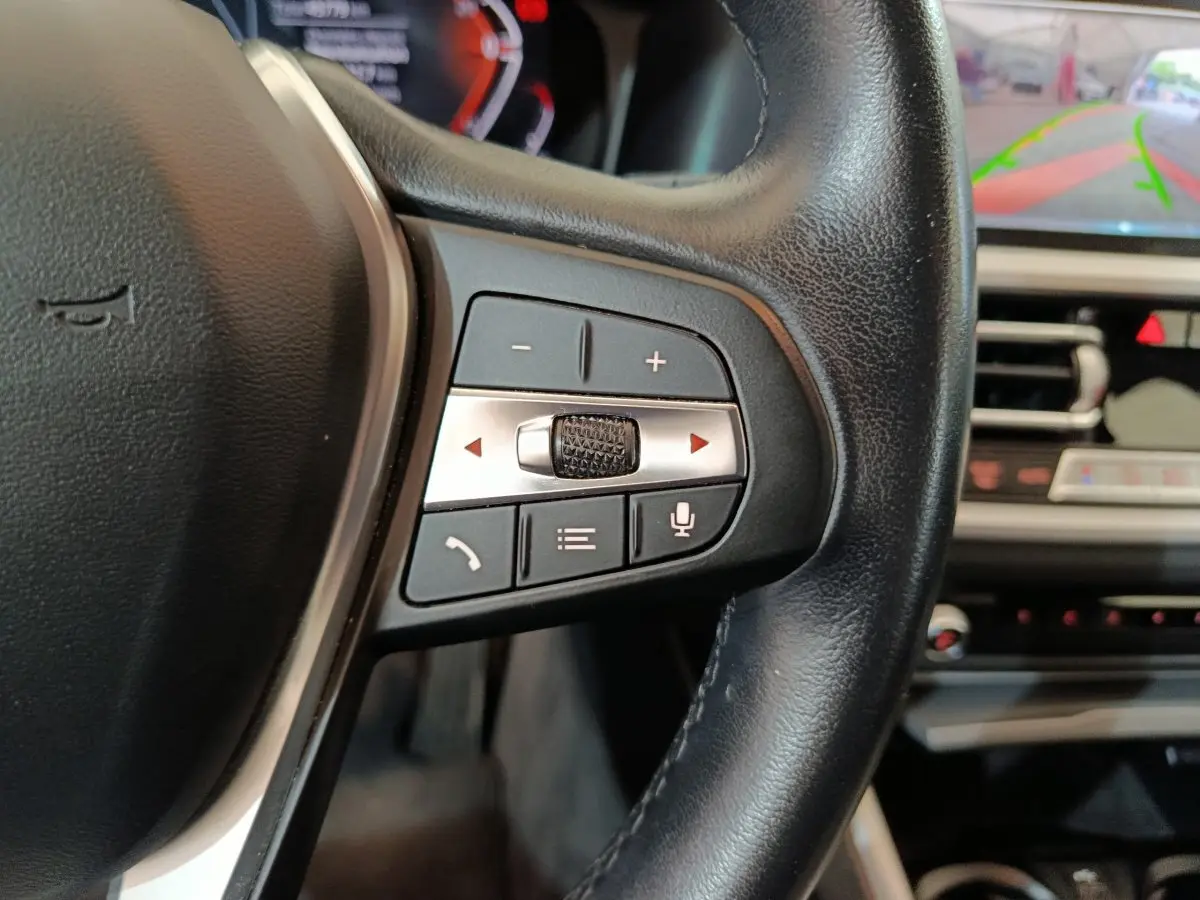 Gros plan sur les commandes du volant à droite de la BMW Série 3 316d gris clair, avec écran tactile et caméra de recul visible.